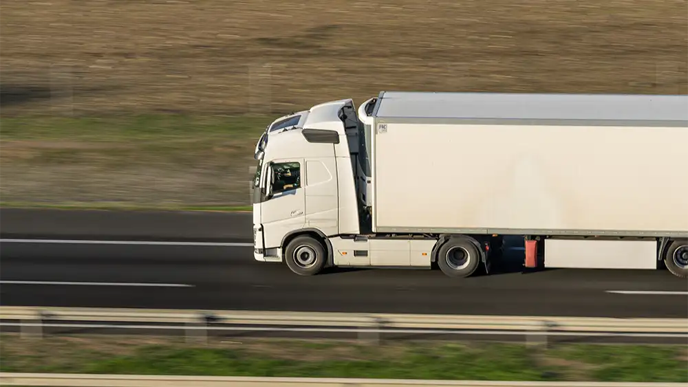 Camión de carga blanco circulando por una autopista, fotografiado en movimiento desde un lateral.