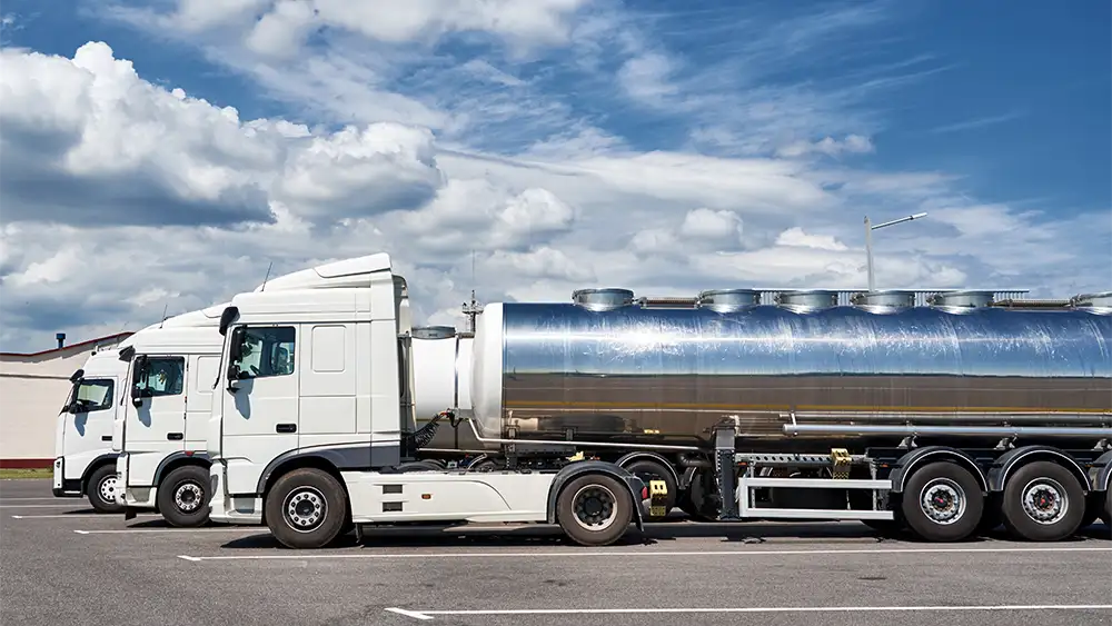 Fila de camiones cisterna blancos estacionados en un aparcamiento industrial bajo un cielo parcialmente nublado.